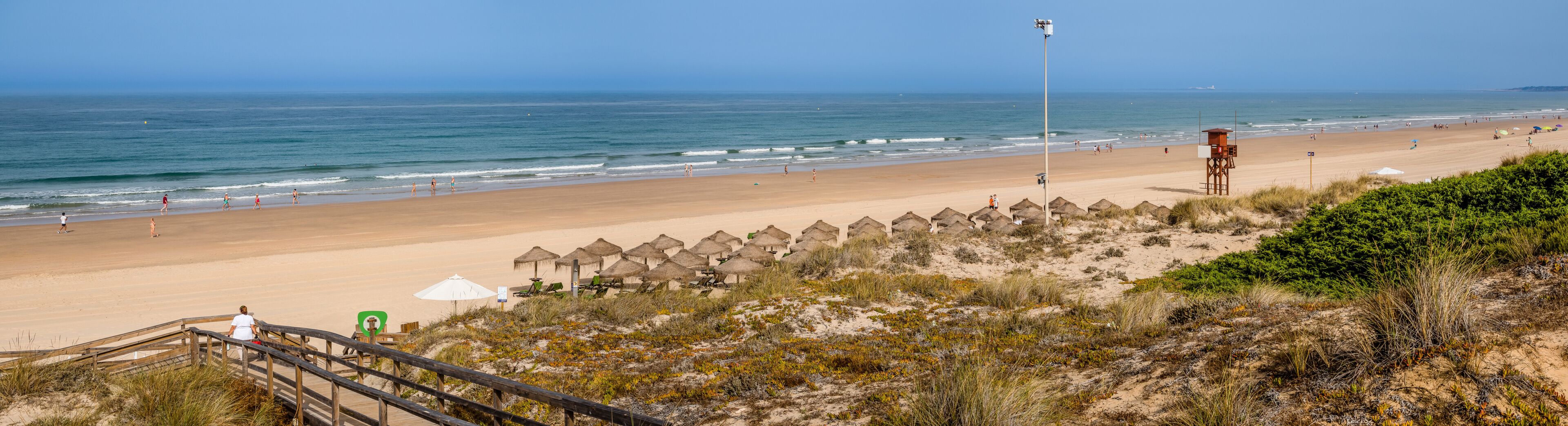 A beach with a lifeguard tower, beach umbrellas, and thatched-roof beach huts.