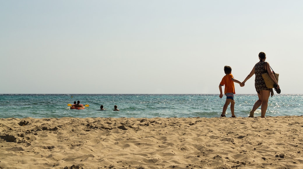 Mother and son holding hands on the beach. People in the sea enjoying the beautiful sunny day at Son Bou beach, located in Menorca, Spain. With copy space.