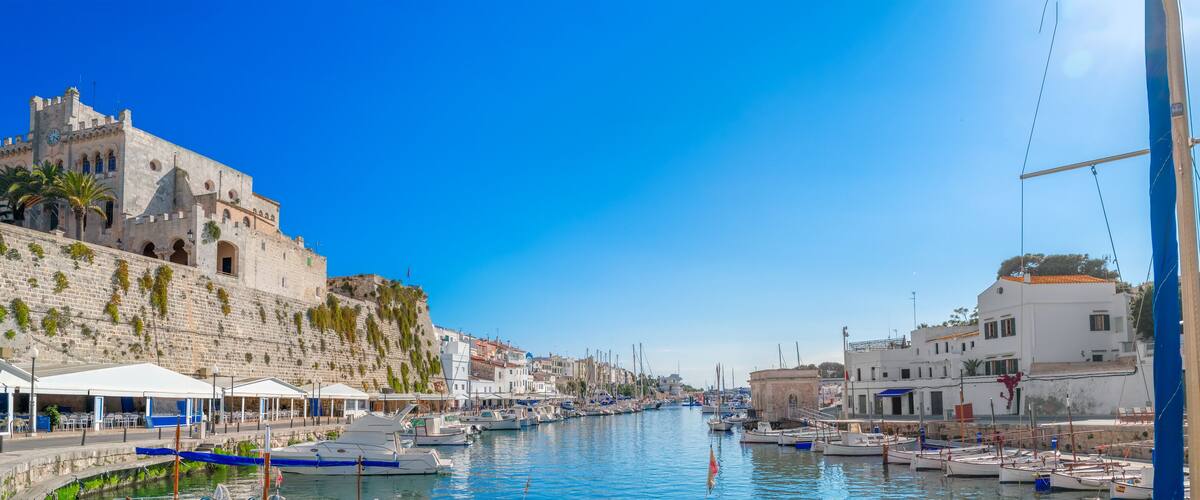 A coastal town with a historic castle, a marina with boats, and white buildings along the waterfront.