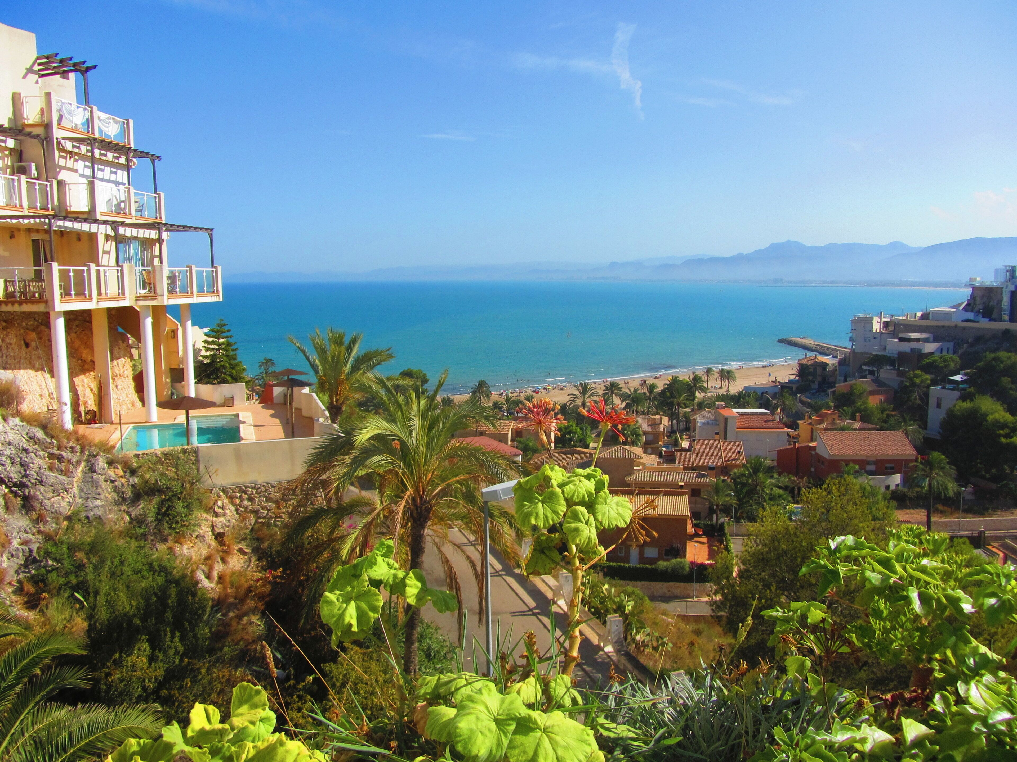 A coastal town with a clear view of the sea, a swimming pool, and lush greenery.