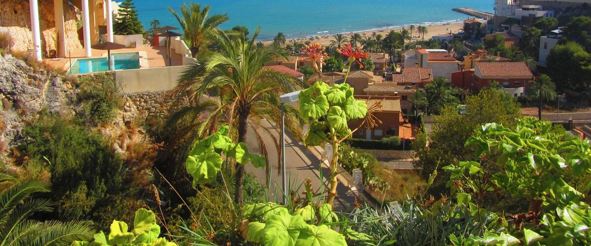 A coastal town with a clear view of the sea, a swimming pool, and lush greenery.