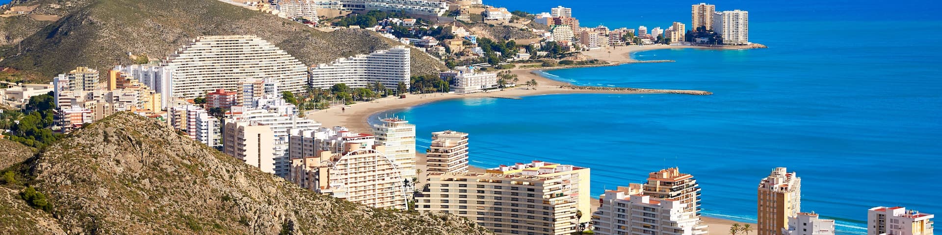 A coastal city with a beach, buildings, and a hill.