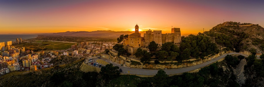 Un castillo histórico en una colina con vistas a una ciudad costera al atardecer.