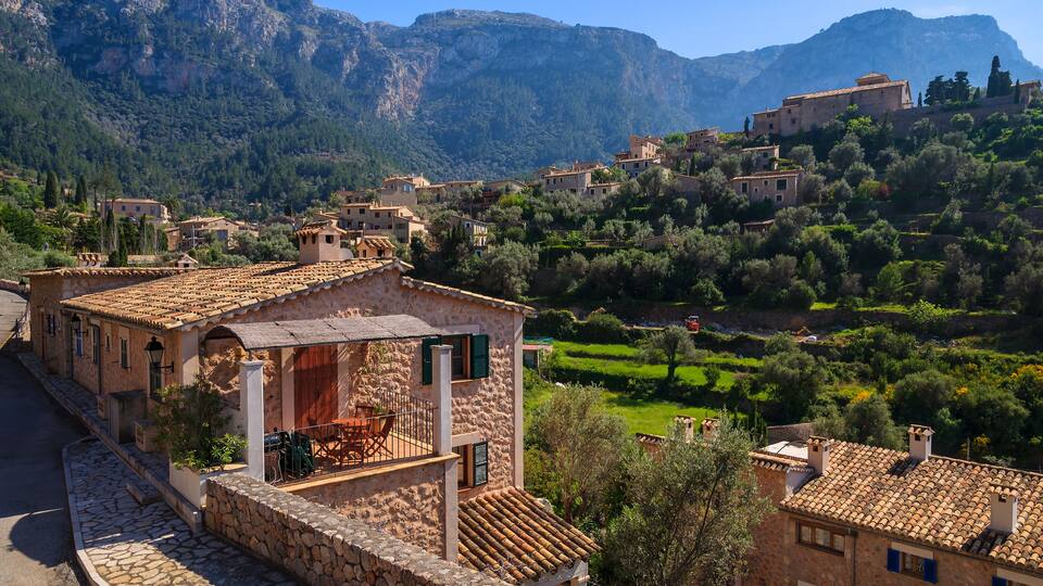 A hillside village with stone buildings, terracotta roofs, and lush greenery.