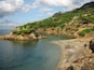 A coastal landscape with rocky cliffs, clear blue water, and green vegetation.