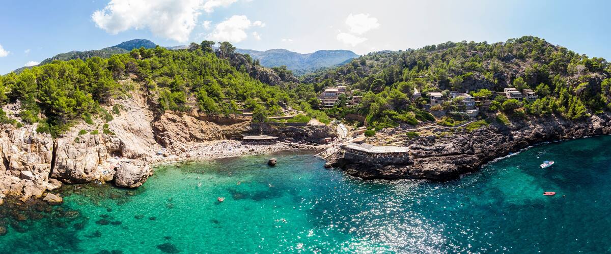 A coastal landscape with clear turquoise waters, rocky cliffs, and scattered buildings.