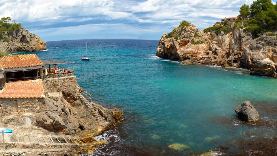 A coastal village with traditional stone buildings, a rocky shoreline, and clear turquoise waters.