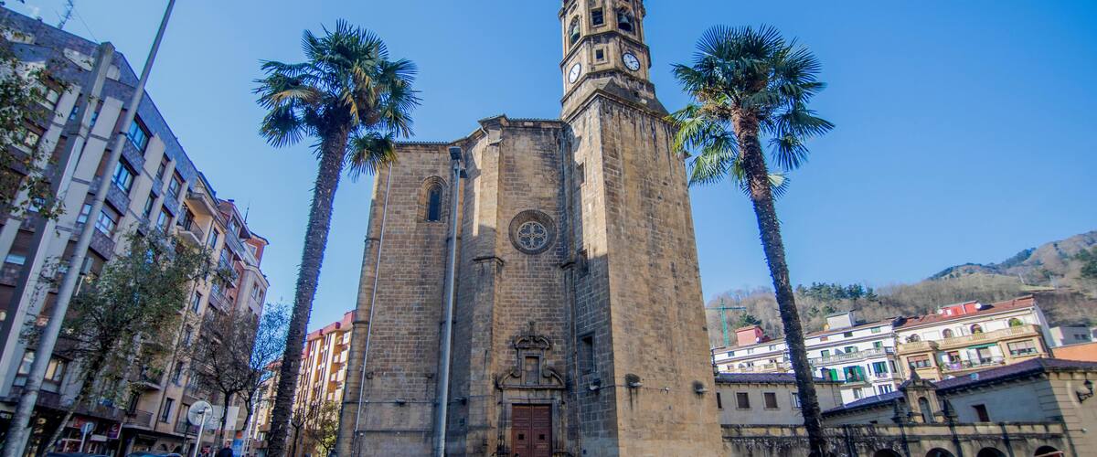 A historic church with a clock tower, surrounded by palm trees and modern buildings.