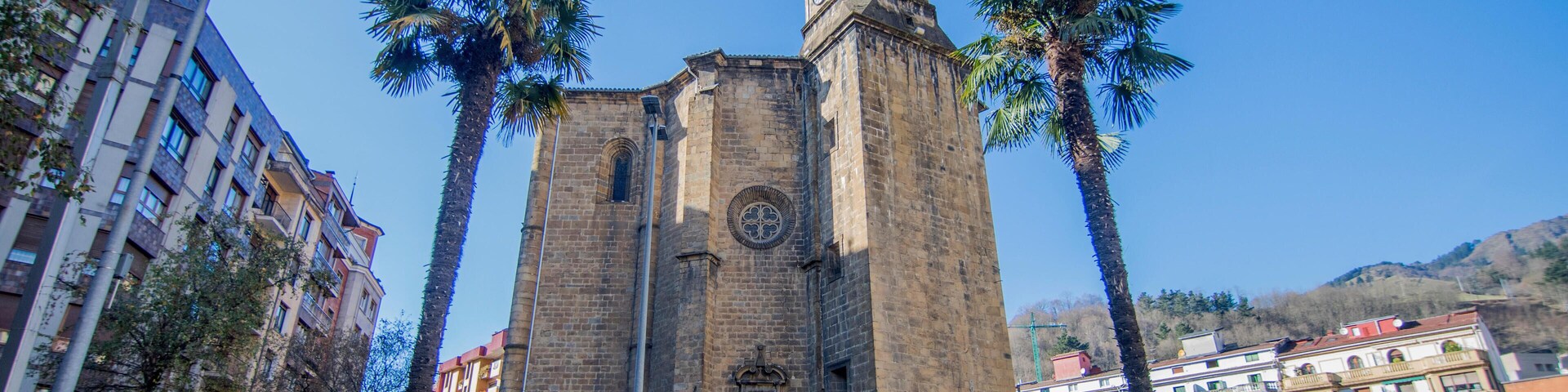 A historic church with a clock tower, surrounded by palm trees and modern buildings.