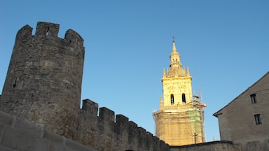 A historic stone tower with a spire, a medieval castle wall, and a modern building.