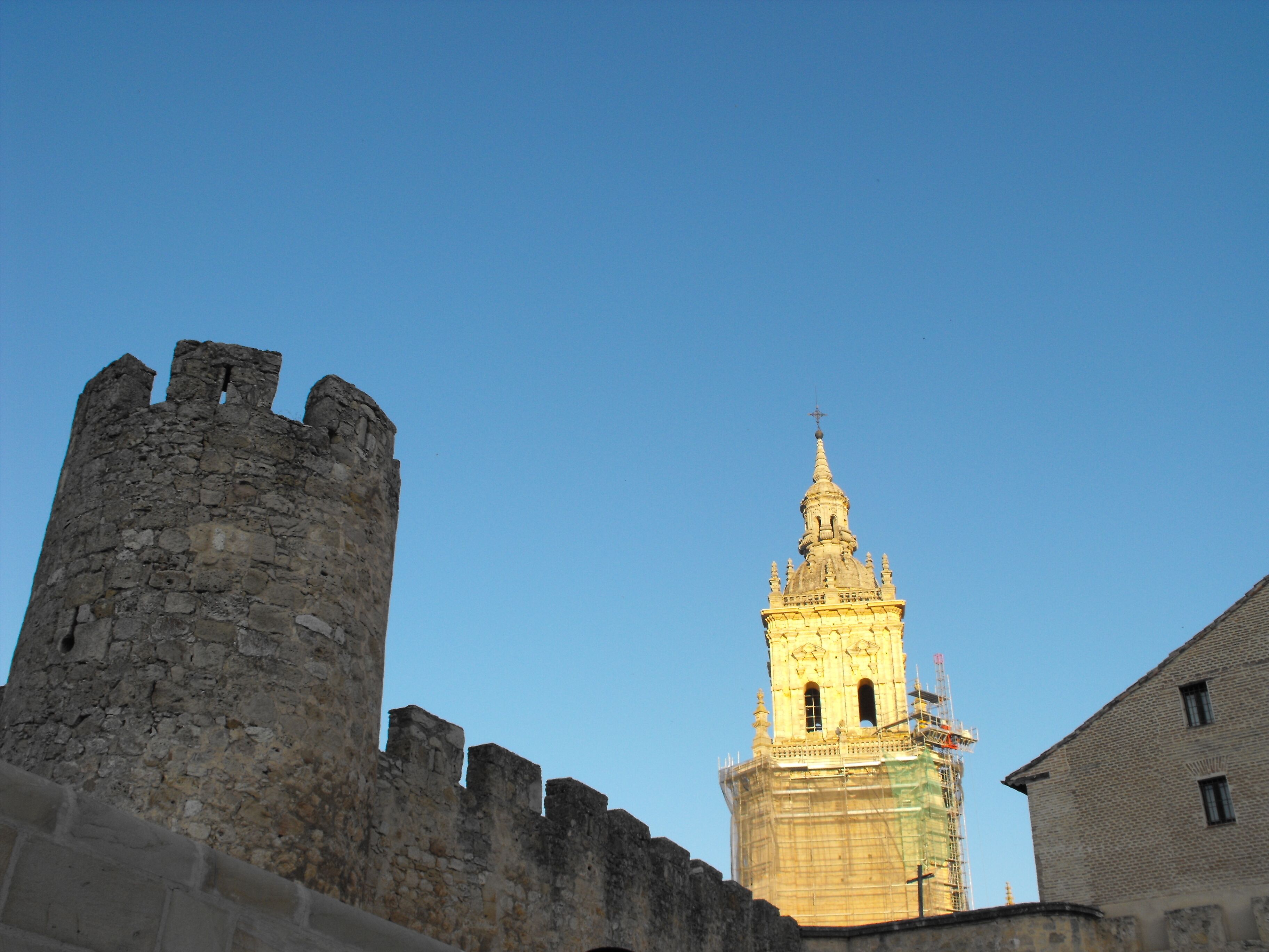 A historic stone tower with a spire, a medieval castle wall, and a modern building.