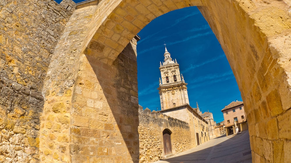 An ancient stone archway framing a view of a historic bell tower and surrounding buildings.