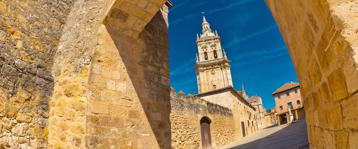 An ancient stone archway framing a view of a historic bell tower and surrounding buildings.