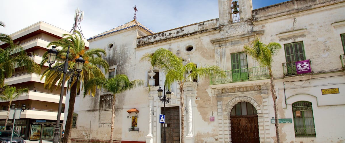 A historic building with a bell tower, palm trees, and a sign for 'Hospital de San Juan de Dios'.