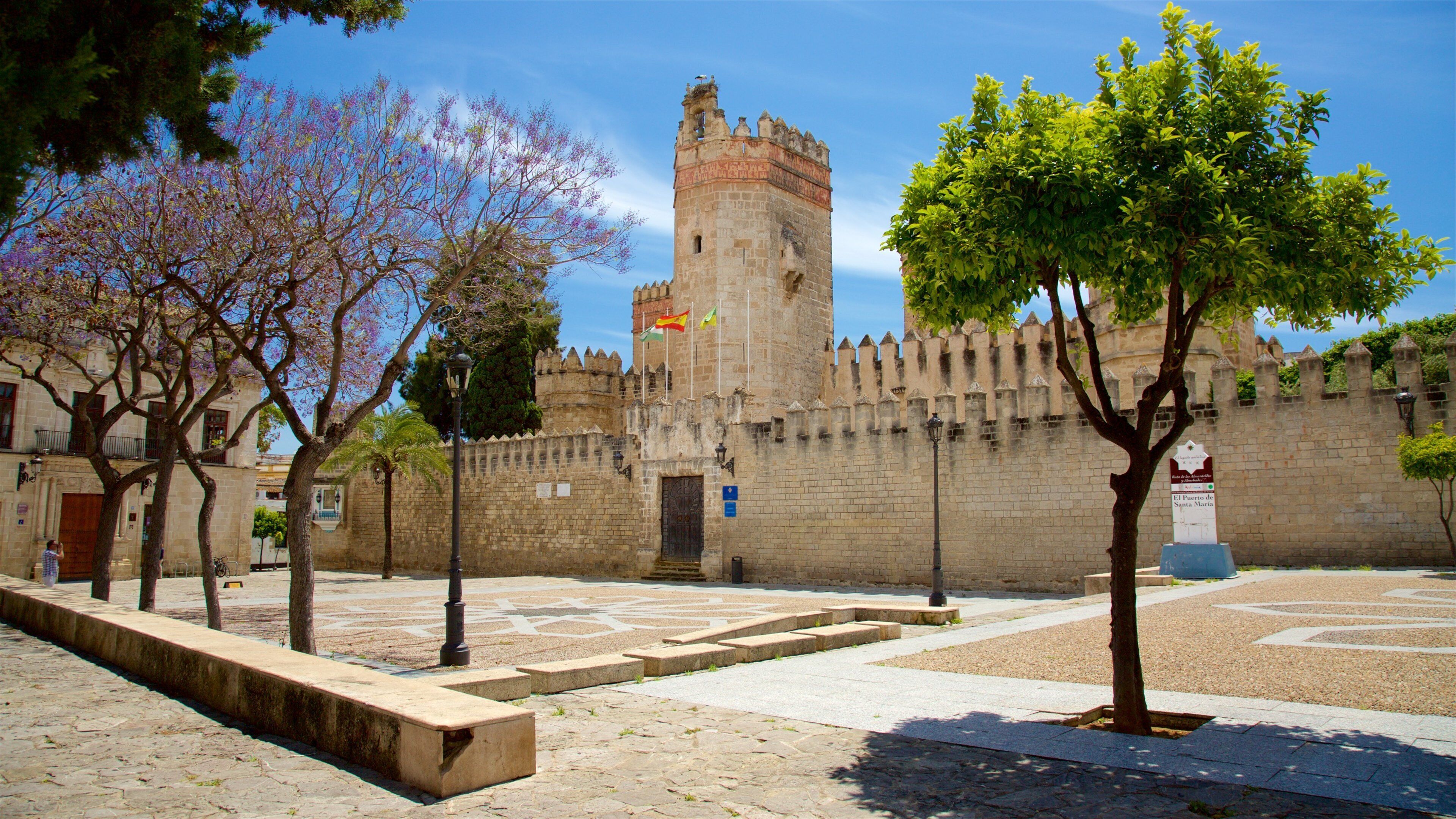 A historic stone fortress with a tall tower, surrounded by trees and a paved courtyard.