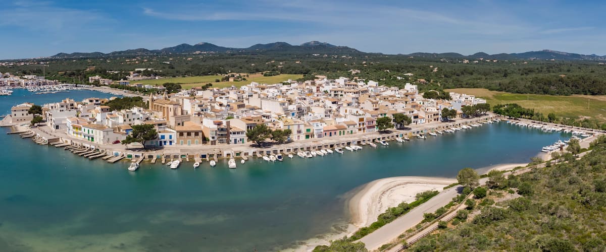 A coastal town with a marina, buildings, and a mountainous backdrop.