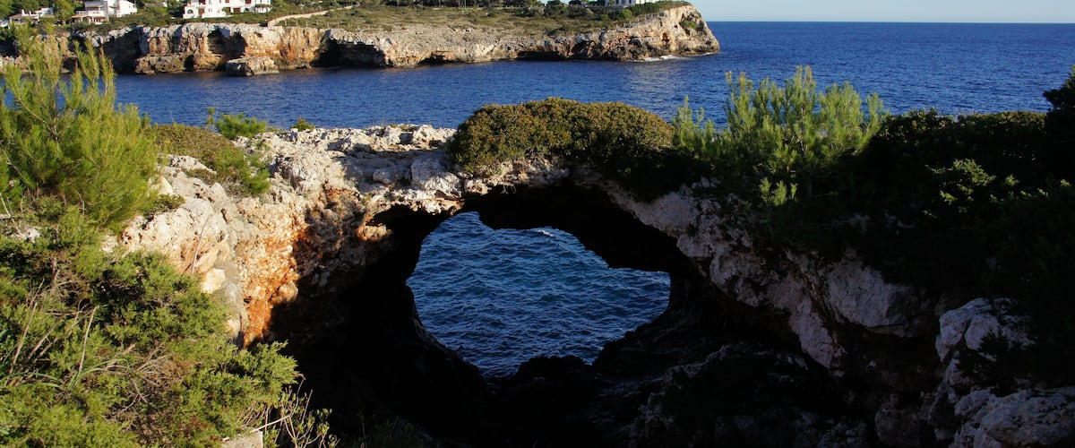 A coastal landscape with a lighthouse, rocky cliffs, and a sea cave.