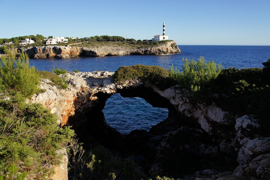 Un paisaje costero con un faro, acantilados rocosos y una cueva marina.