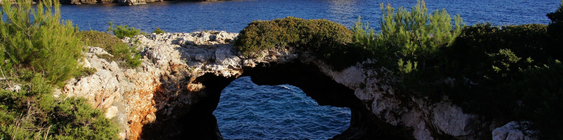 Un paisaje costero con un faro, acantilados rocosos y una cueva marina.