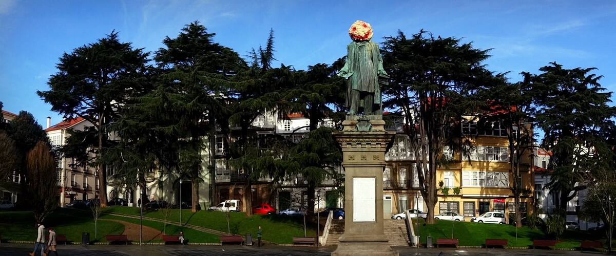 A statue with a large head and a tall, narrow body, surrounded by trees and buildings.