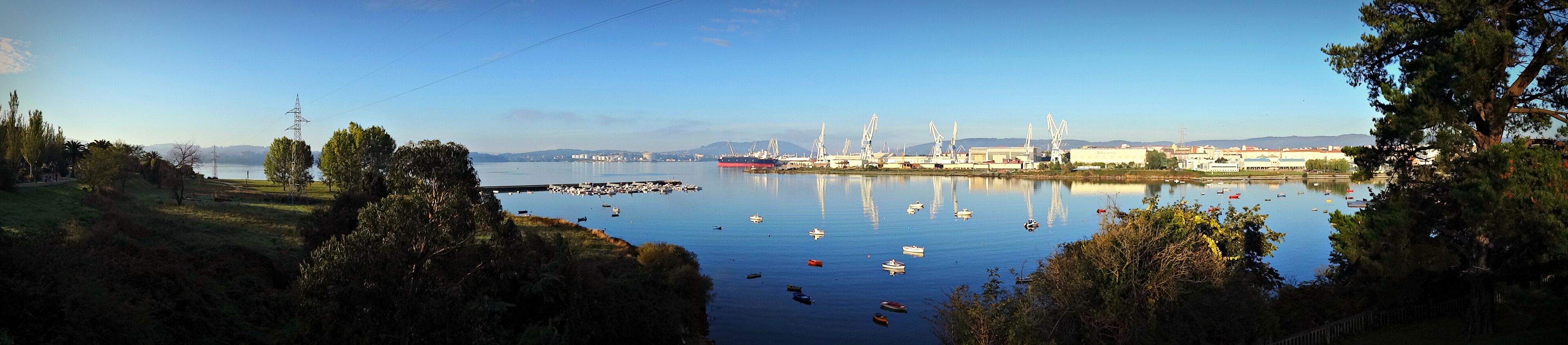 A calm harbor with boats, cranes, and industrial buildings.