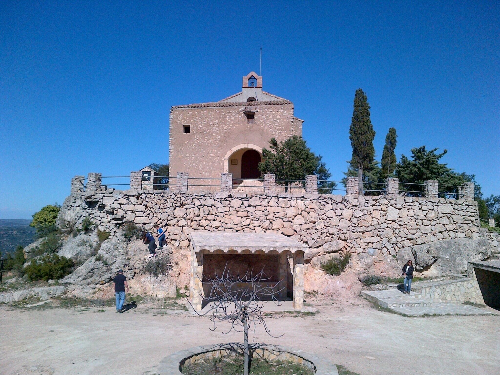 A stone fortress with a central tower, surrounded by a stone wall and a few visitors.