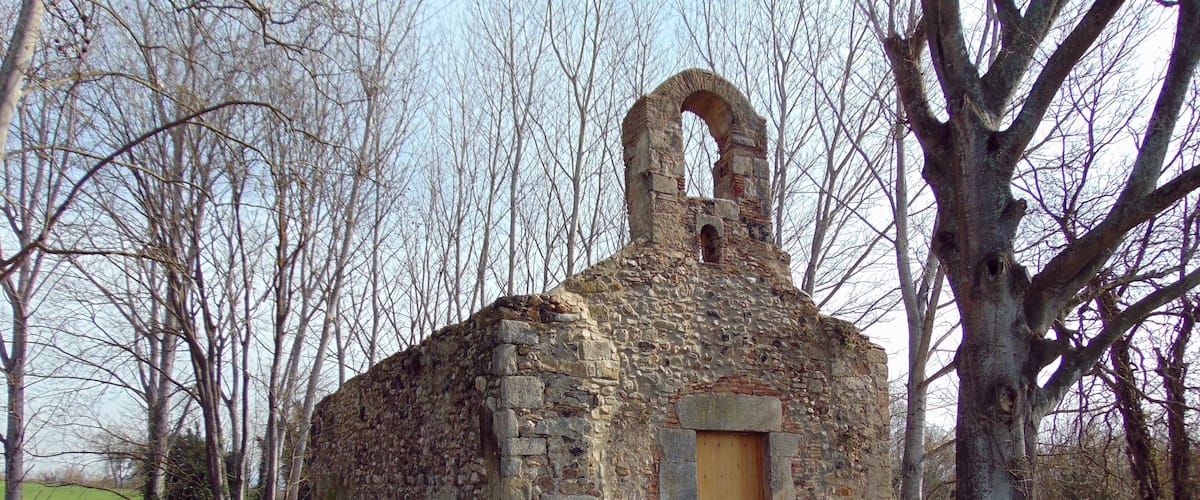A stone church with a wooden door and a bell tower, surrounded by trees and grass.