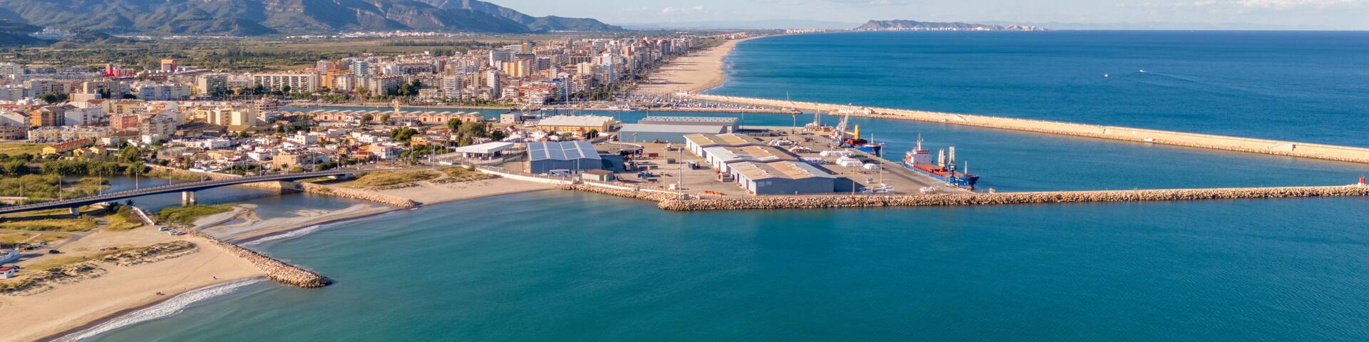 A coastal cityscape with a beach, port, and mountains in the background.