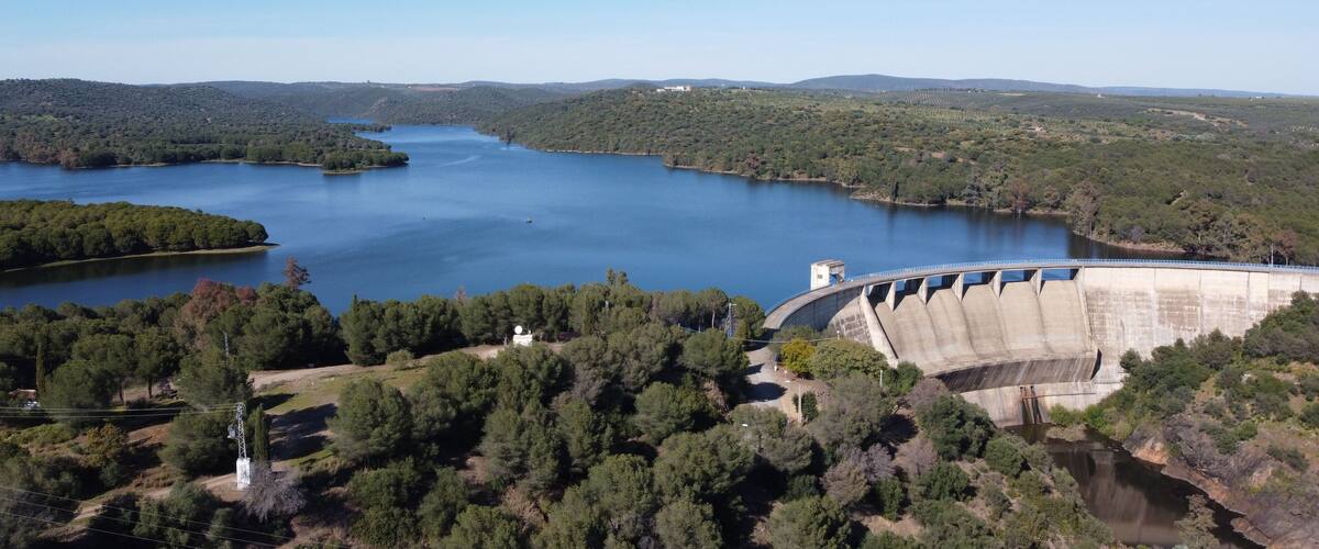 A large dam with a reservoir and surrounding forested hills.