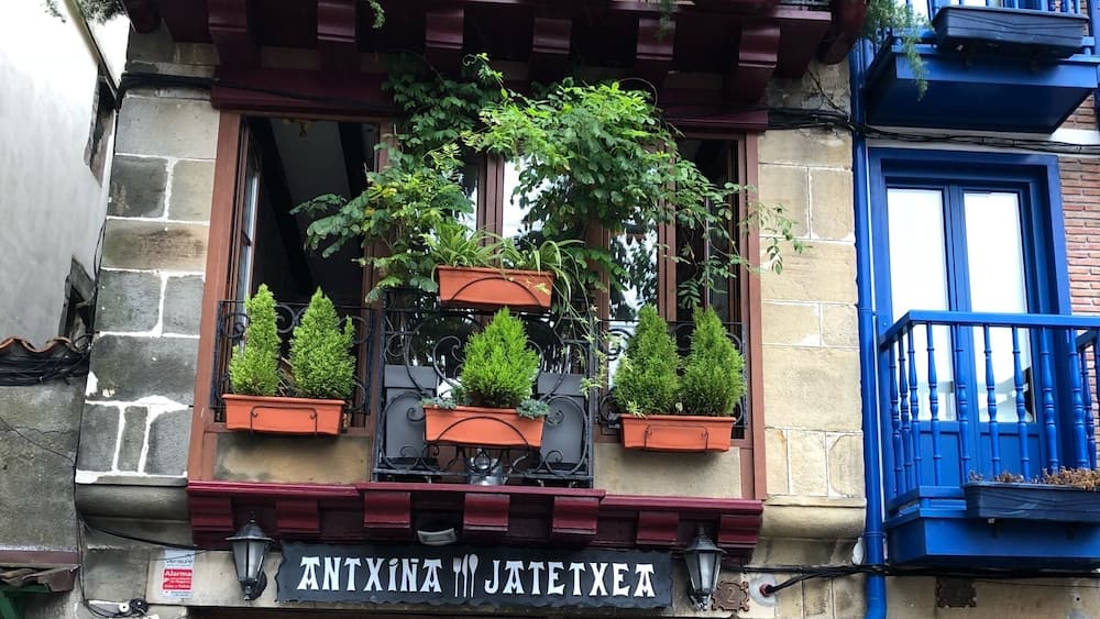Ein Gebäude mit einer Holztür, einem Schild mit der Aufschrift 'ANTXINA JATETXEA' und einer blauen Tür zur Rechten.