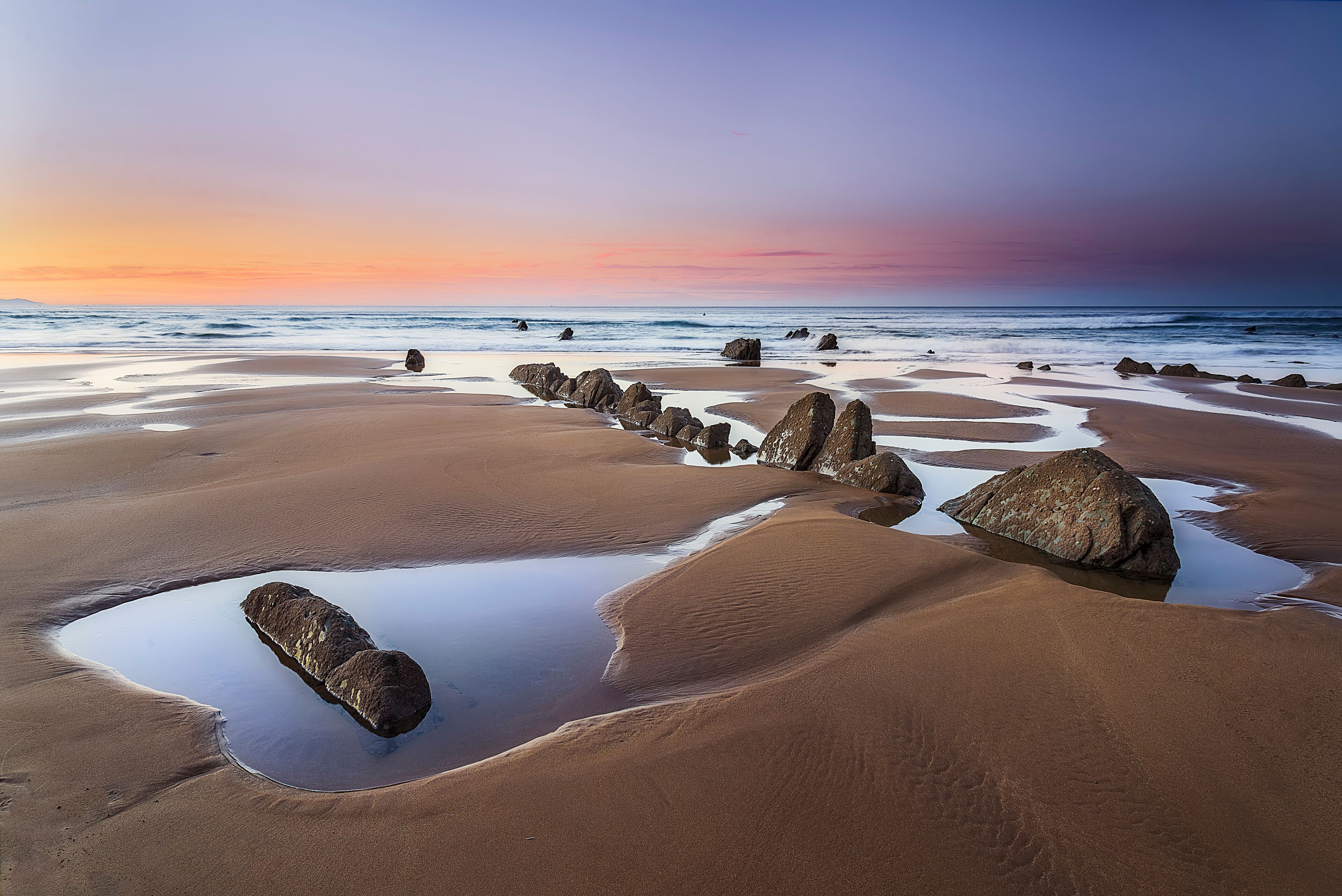 A beach with large rocks and a calm sea at sunset.