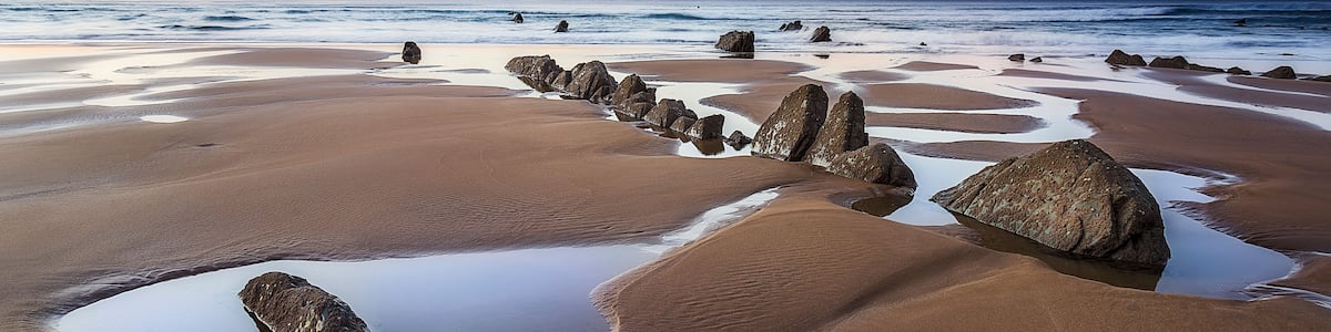 A beach with large rocks and a calm sea at sunset.