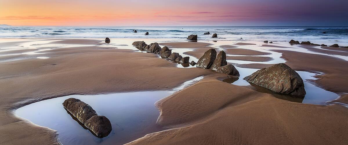 Una playa con rocas grandes y un mar tranquilo al atardecer.