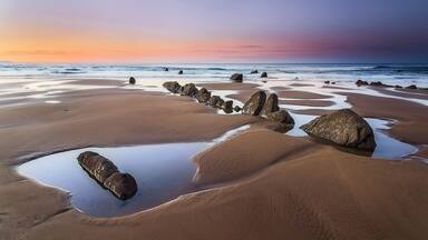 Una playa con rocas grandes y un mar tranquilo al atardecer.