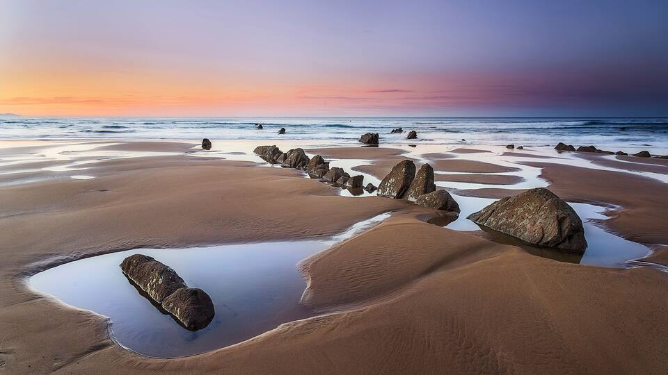 A beach with large rocks and a calm sea at sunset.