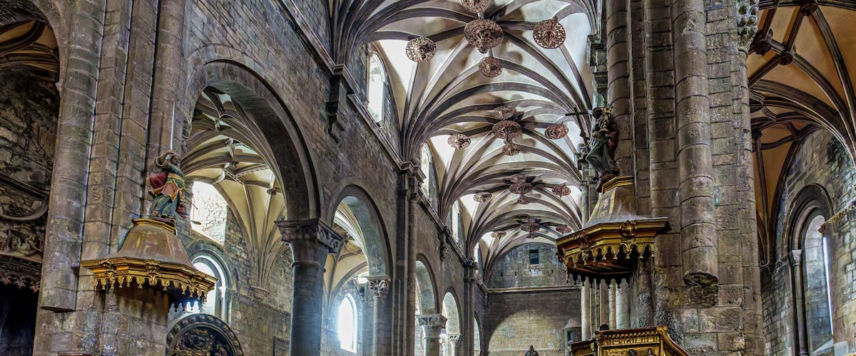 A cathedral interior with high vaulted ceilings, arched windows, and ornate wooden pews.