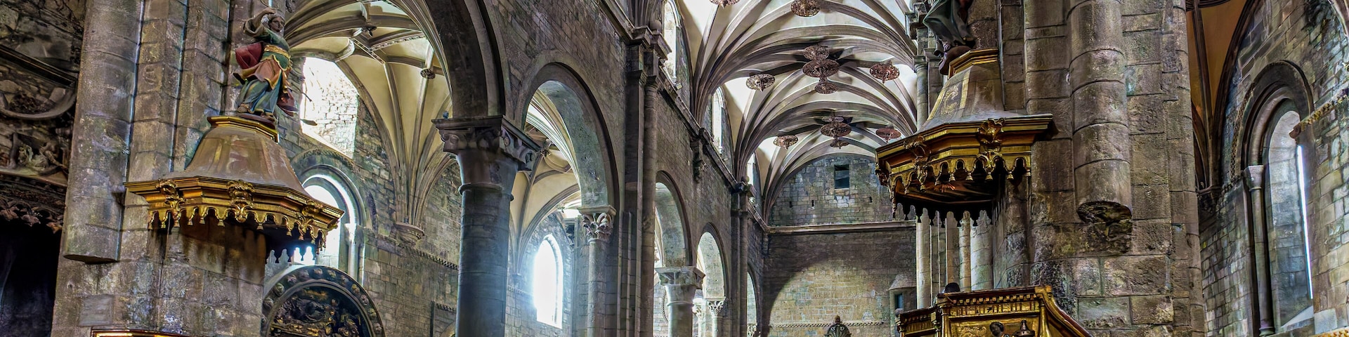 A cathedral interior with high vaulted ceilings, arched windows, and ornate wooden pews.