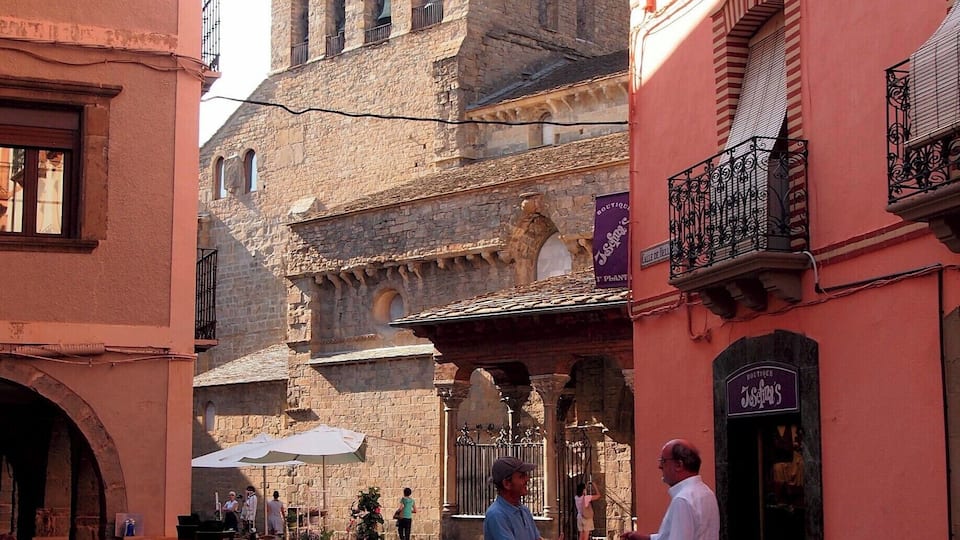 A historic square with stone buildings, a bell tower, and outdoor seating areas.