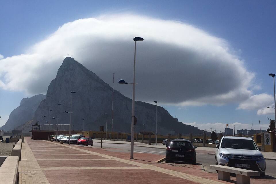 Une montagne surmontée d’une formation nuageuse, une route asphaltée et des voitures garées.