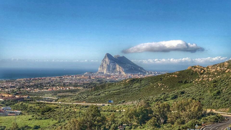 A coastal city with a prominent mountain peak, lush greenery, and a winding road.