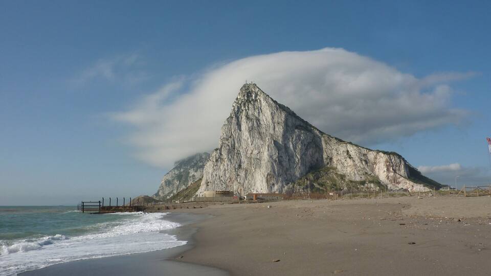 A beach with a large rock formation and a clear sky.
