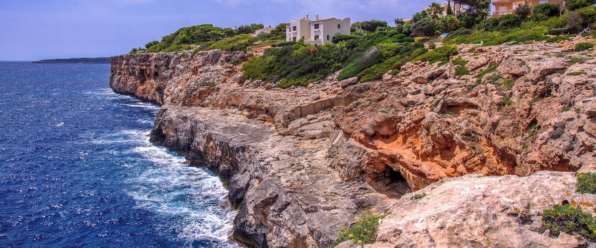 A coastal cliff with a white building and lush greenery.