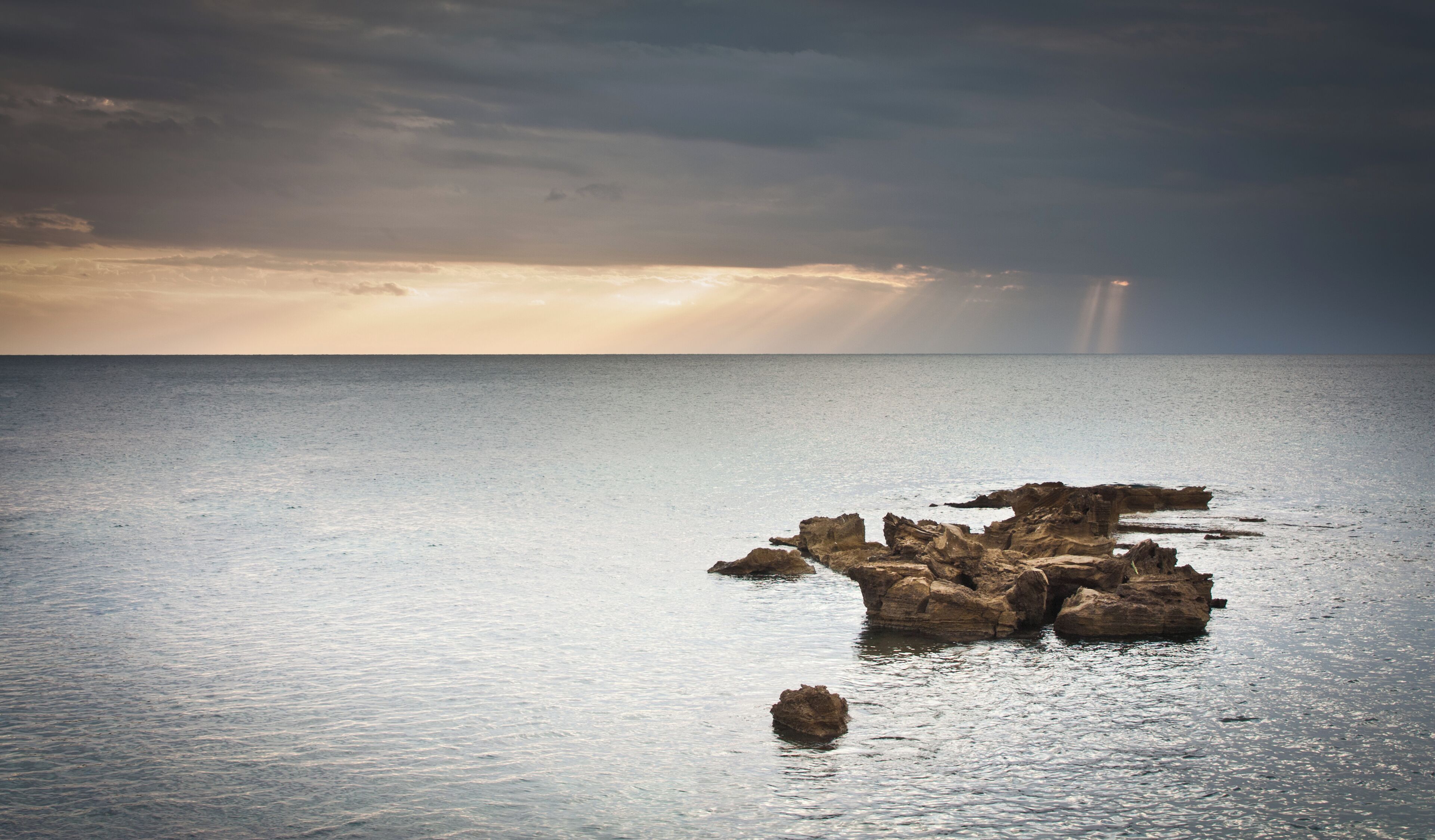 A rocky outcrop in calm waters with a sunset in the background.