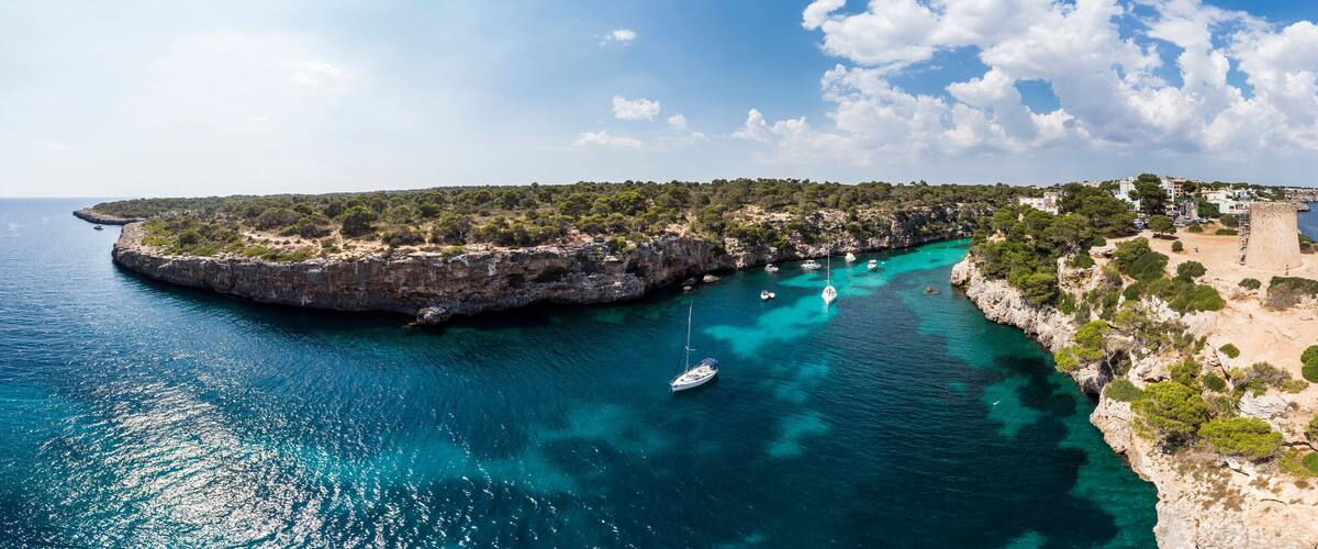 A coastal landscape with a rocky peninsula, clear turquoise waters, and a small boat anchored near the shore.