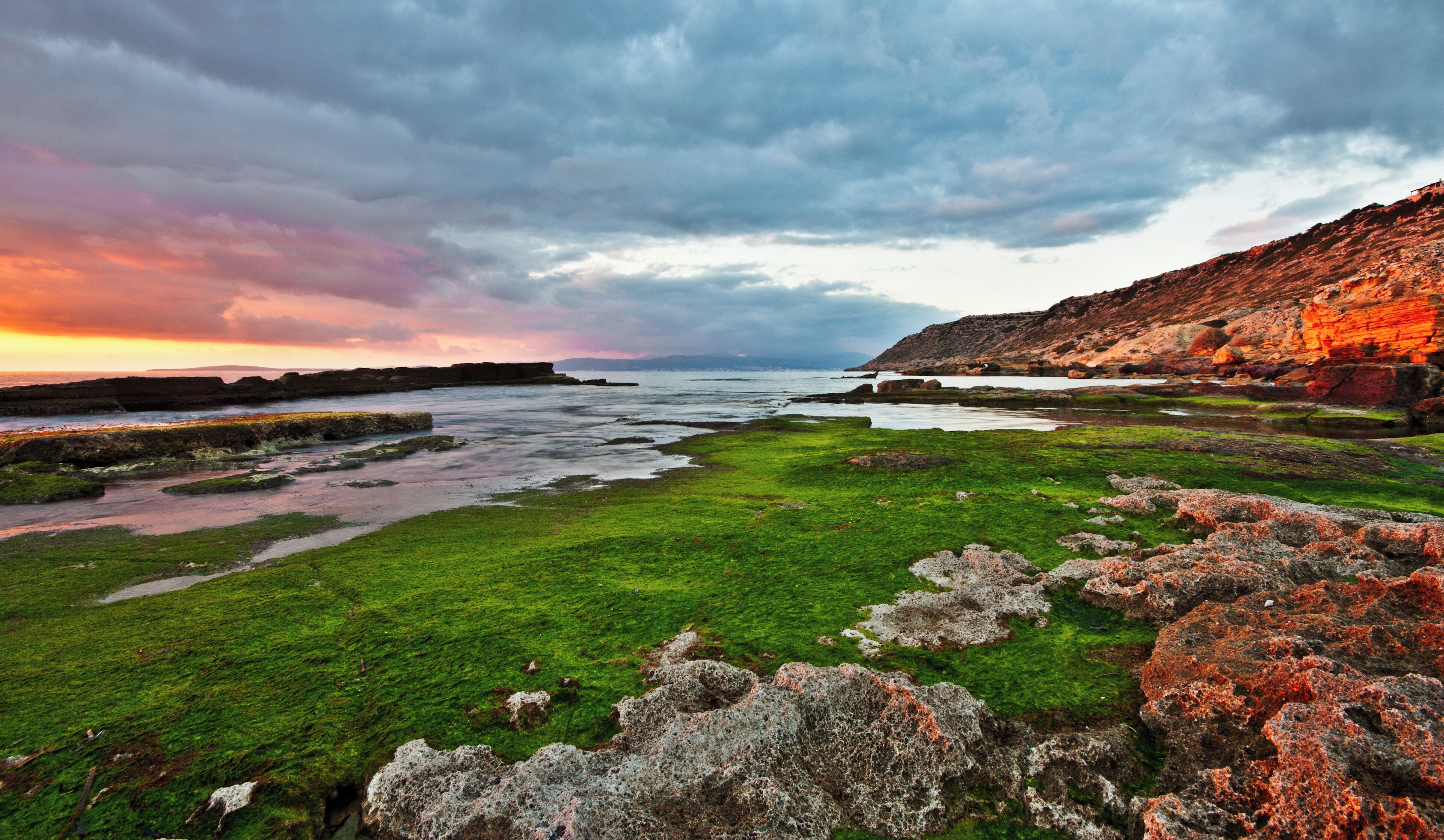 Un paisaje costero con musgo verde, afloramientos rocosos y un cielo de atardecer espectacular.