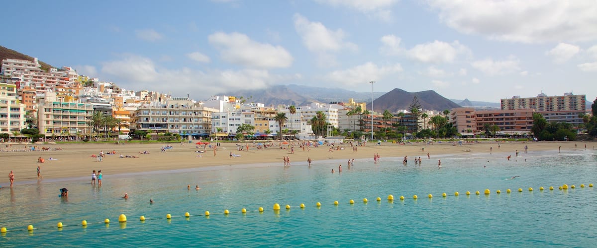A beach with clear turquoise water, people sunbathing, and buildings in the background.