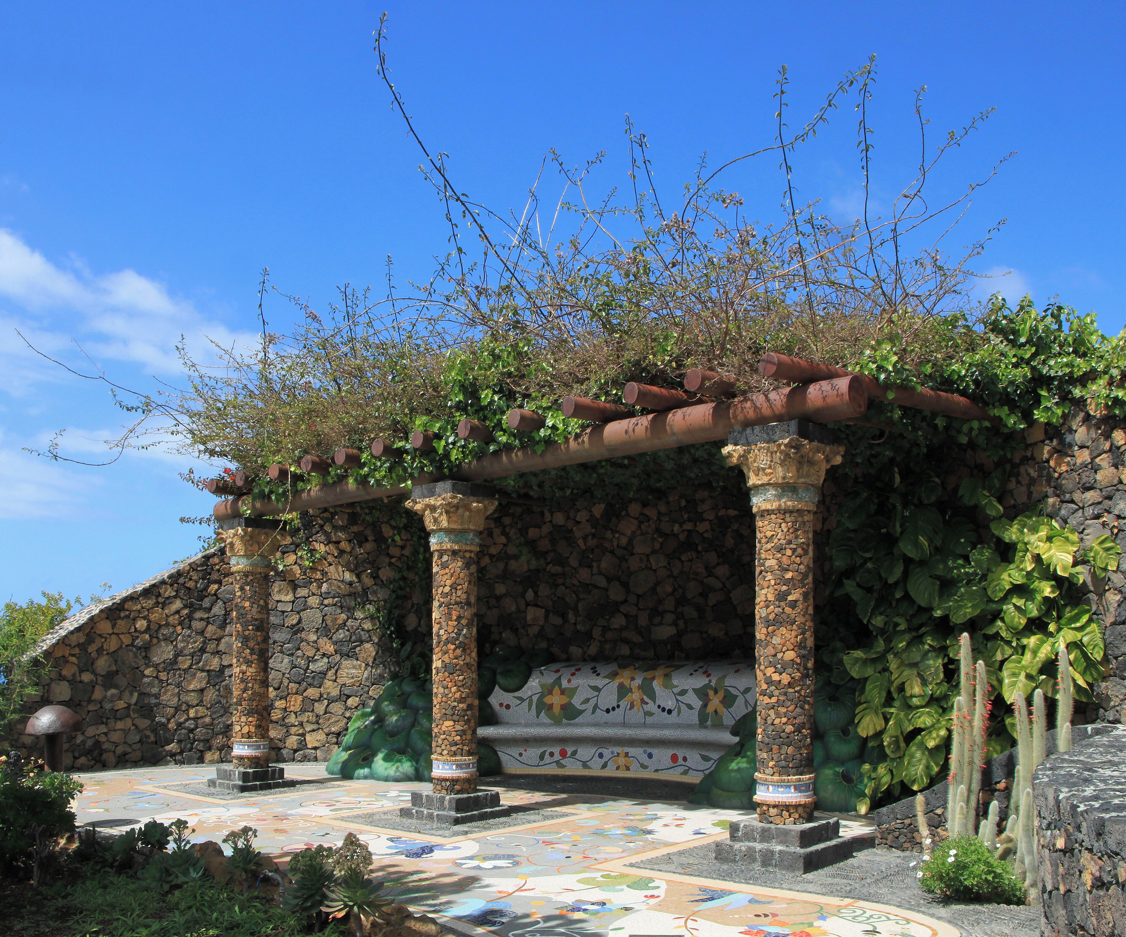 A stone structure with columns, a tiled floor, and a pergola covered in vines.