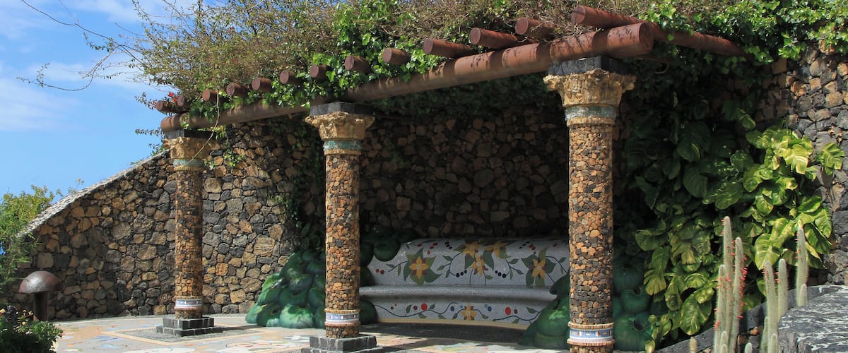 A stone structure with columns, a tiled floor, and a pergola covered in vines.