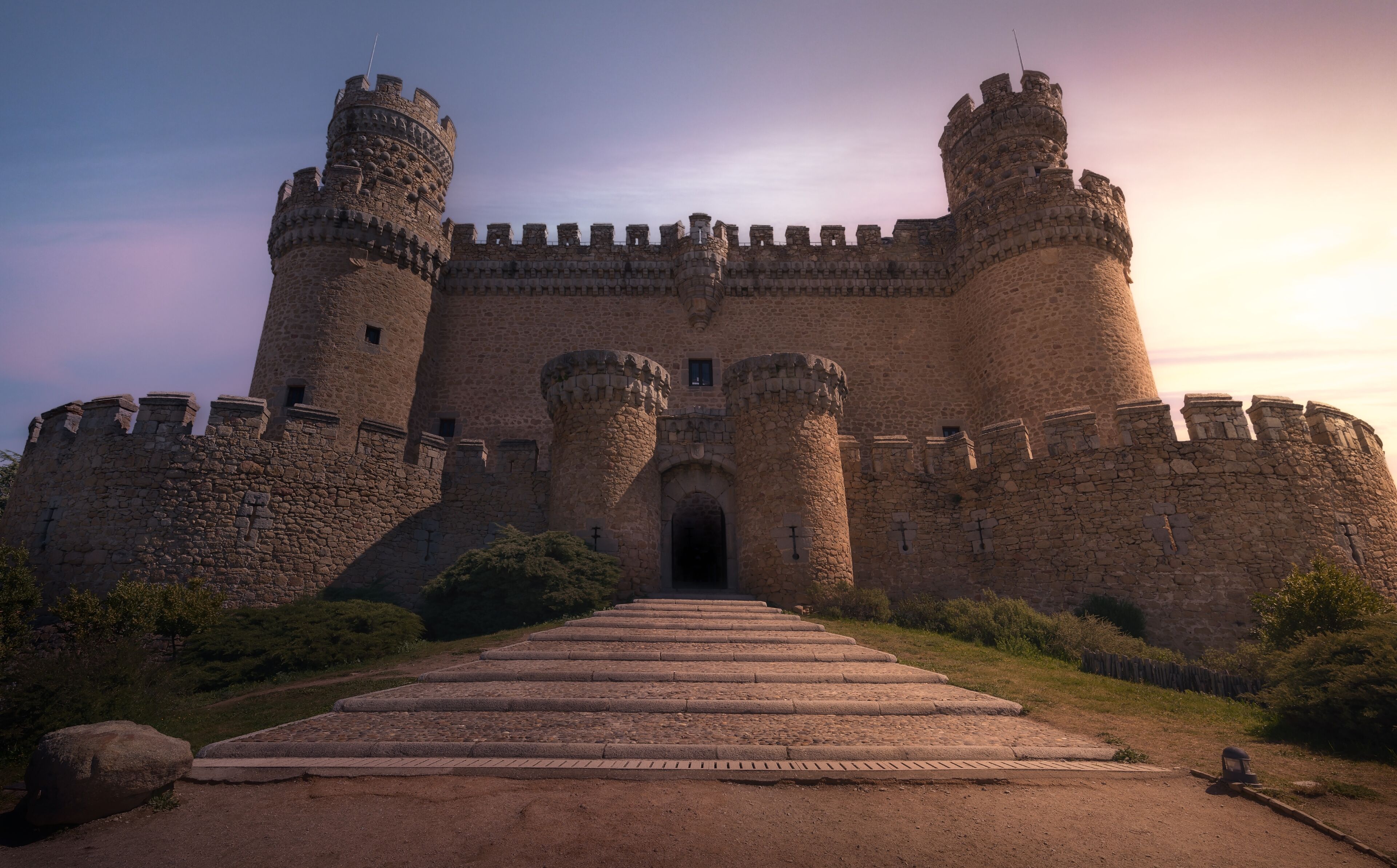 A medieval castle with two large towers, a central entrance, and a stone pathway leading to the gate.