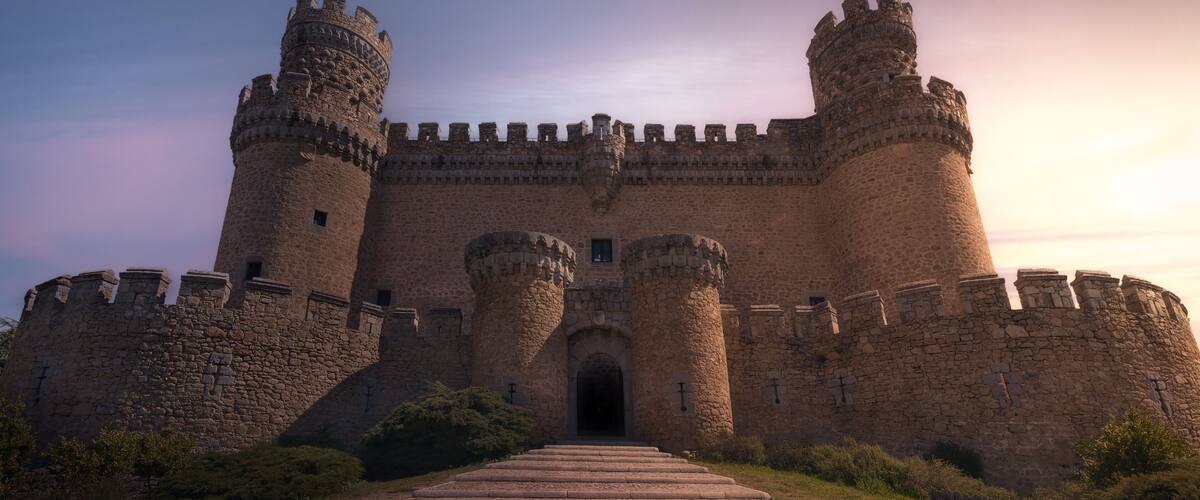 A medieval castle with two large towers, a central entrance, and a stone pathway leading to the gate.